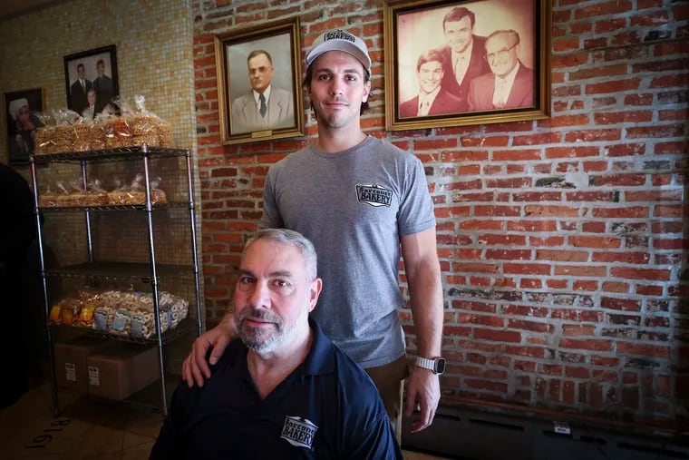 Lou Sarcone, a fourth generation baker, poses for a portrait with his son, Louis, with family photos behind them at Sarcone's Bakery in South Philadelphia on March 8. The Sarcones are one of Philly’s best-known baking families. Lou Sarcone is stepping away from the ovens due to his Parkinson's disease. His son, Louis, is taking over.