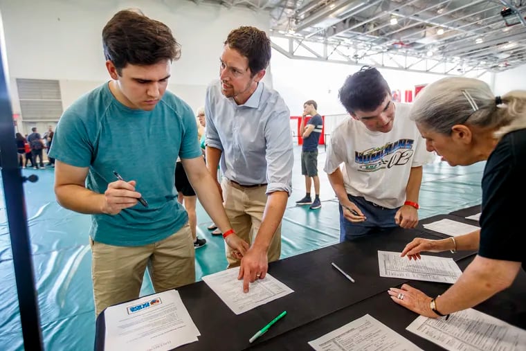 Incoming Haverford College freshman Matthew Dodds, left, from Princeton, N.J., gets help from Haverford professor Zachary Oberfield, center, in filling out his voter registration form on the first day check-in for freshman at Haverford on August 29, 2018. This year, voter registration has fallen significantly as the pandemic restricted activity.