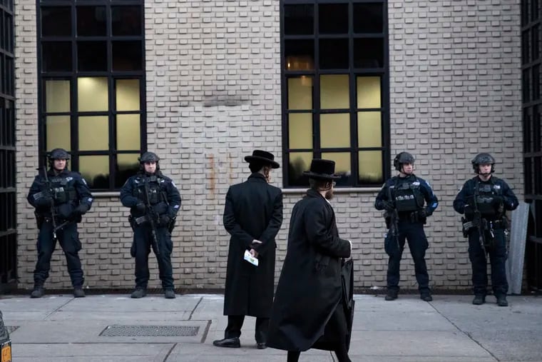 Orthodox Jewish men pass New York City police guarding a Brooklyn synagogue prior to a funeral for Mosche Deutsch, Wednesday, Dec. 11, 2019 in New York. Deutsch, a rabbinical student from Brooklyn, was killed Tuesday in the shooting inside a Jersey City, N.J. market.
