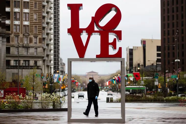 A person wearing a protective face mask and gloves as a precaution against the coronavirus walks by the Robert Indiana sculpture "LOVE" at John F. Kennedy Plaza, commonly known as Love Park, in Philadelphia, Monday, April 13, 2020. The sculpture is a big attraction for tourists. (AP Photo/Matt Rourke)