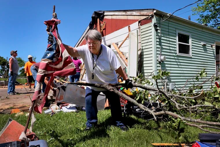 Patti Manley, 69, moves a shredded American flag as she gathers branches from the backyard of her mother's home on Morningdale Place in Mehlville, Mo., on Monday, May 27, 2024, following a violent storm and possible tornado Sunday evening. Manley was staying with her mother Jackie Moloney, 88, when the storm hit. She and her mother rode it out in an interior bathroom.