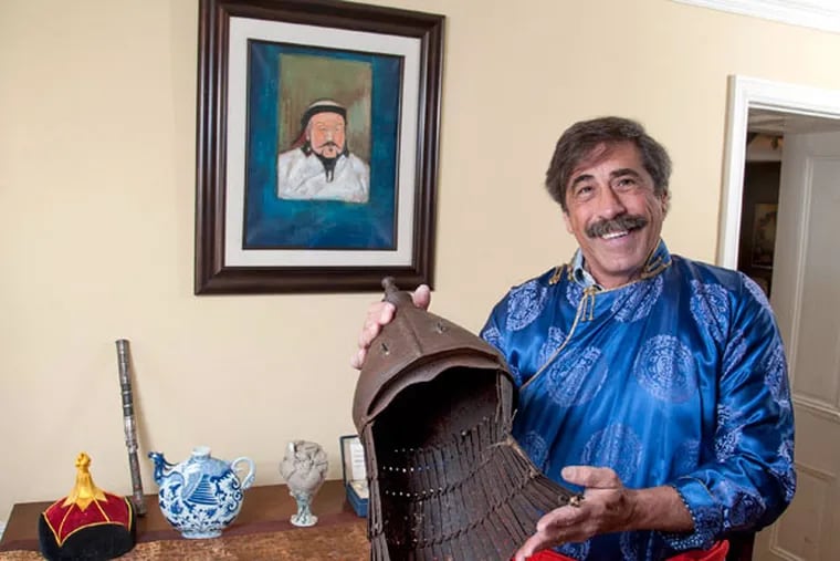 Don “Dino Don” Lessem shows off his Mongolian robe and a 14th-century Mongolian warrior helmet in front of a painting of Genghis Khan, the star of his traveling exhibit. (CLEM MURRAY / STAFF PHOTOGRAPHER)