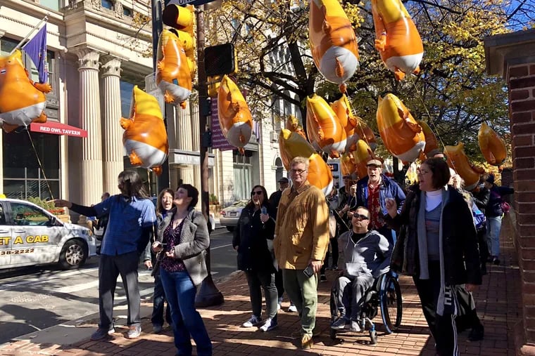 A group of balloon-wielding protesters walks west on Chestnut Street led by Claude Taylor, the founder of the Mad Dog PAC. Taylor is in the center in a tan jacket.