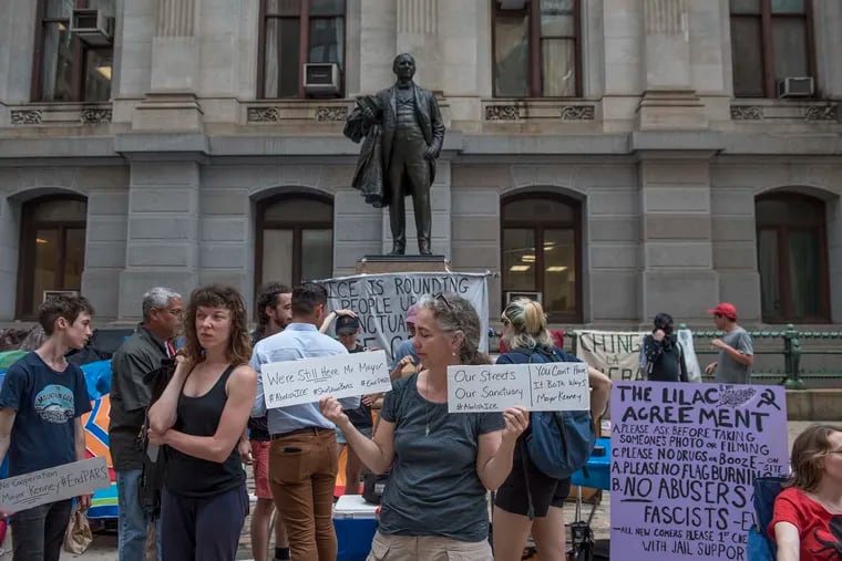 Alison McDowell, right, holds up two signs during the Occupy ICE protest on the east side of City Hall on Friday.