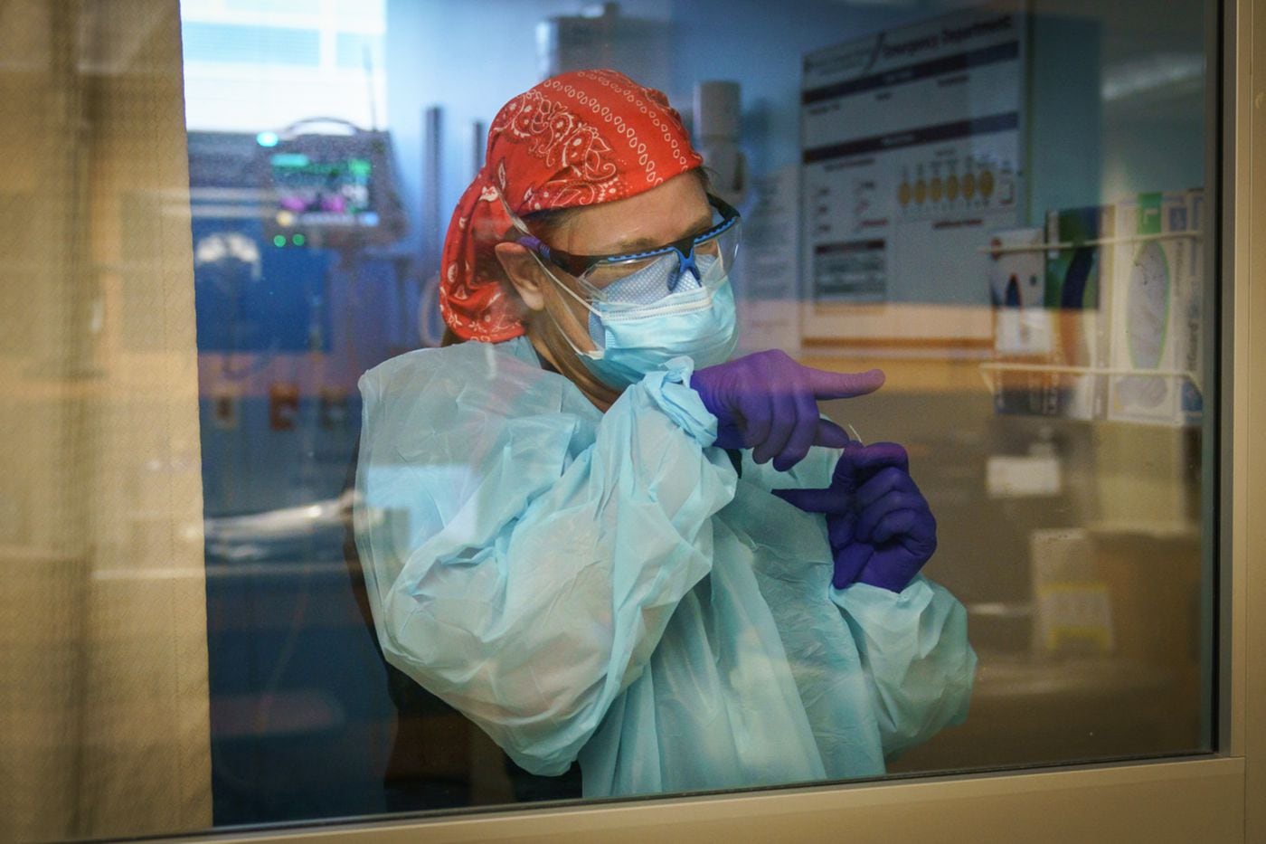 Nurse Sherry Seymour gestures to a colleague to request supplies while treating a COVID-19 patient inside a glass-enclosed ER bay at Suburban Community Hospital. 