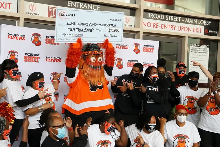 Gritty holds up a ceremonial check as he poses with members of the Black Doctors COVID-19 Consortium at the consortium's vaccination clinic at the Liacouras Center in April. The Flyers donated $10,000 to the consortium, which will use the money to support ongoing efforts to vaccinate homebound individuals.