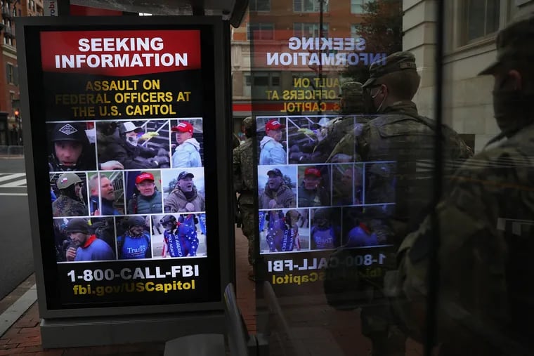 National Guard members walk past a bus station screen displaying pictures of people suspected of participating in the Capitol riot, as seen on the day before the presidential inauguration of Joe Biden in Washington, D.C., on Tuesday, Jan. 19, 2021.