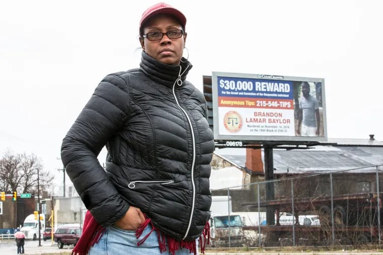 Mykia Capers stands near the corner of West Glenwood Avenue and North 29th Street, beside a billboard announcing a reward for information leading to the arrest and conviction of her son’s murderer.