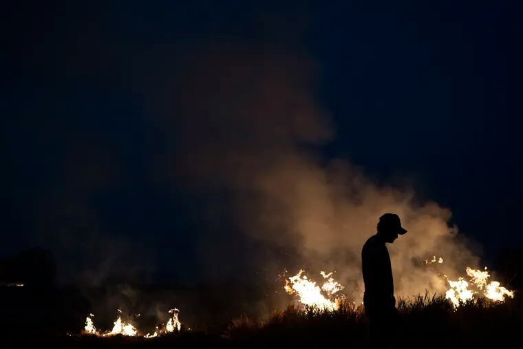 Neri dos Santos Silva, center, is silhouetted against an encroaching fire threat after he spent hours digging trenches to keep the flames from spreading to the farm he works on, in the Nova Santa Helena municipality, in the state of Mato Grosso, Brazil, Friday, Aug. 23, 2019. Under increasing international pressure to contain fires sweeping parts of the Amazon, Brazilian President Jair Bolsonaro on Friday authorized use of the military to battle the massive blazes.