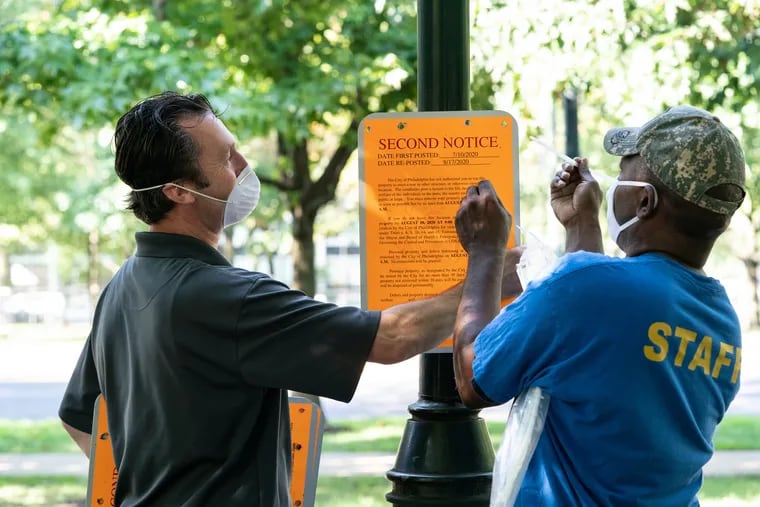 City employees post a notice saying the homeless encampment on the Benjamin Franklin Parkway will be cleared out by 9 a.m. Tuesday. It was the city's second notice of closure, the first, on July 10, having been postponed by Mayor Jim Kenney in an effort to extend negotiations with encampment organizers. On Monday, Kenney declared the talks "fruitless."