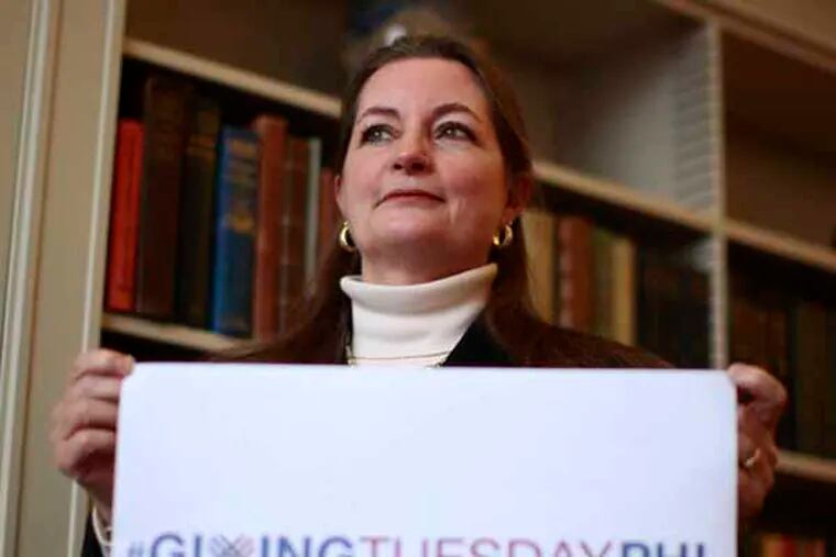 Siobhan A. Reardon, president and director of the Free Library of Philadelphia, poses with a large placard that advertising Giving Tuesday - a day to give after a weekend of shopping. November 27, 2013. ( DAVID SWANSON / Staff Photographer )