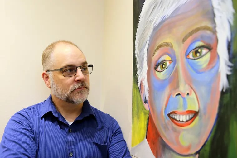 George Semple poses next to a self portrait of his late wife, Lisa, at the Cherry Hill Library in Cherry Hill. She made portraits of fellow cancer patients before she died.