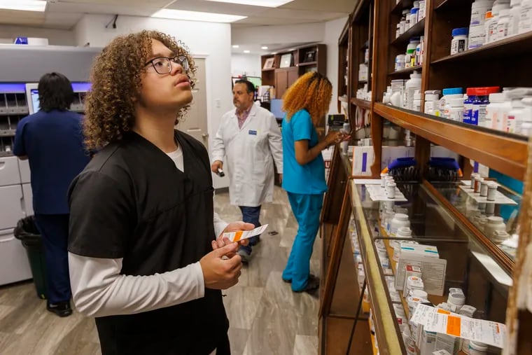 Christian Watson, 17, looks for medication to fill a prescription. Students from Brimm Medical Arts High School are getting training at the Bell Pharmacy, 1201 Haddon Avenue, Camden on Wednesday morning April 26, 2023,