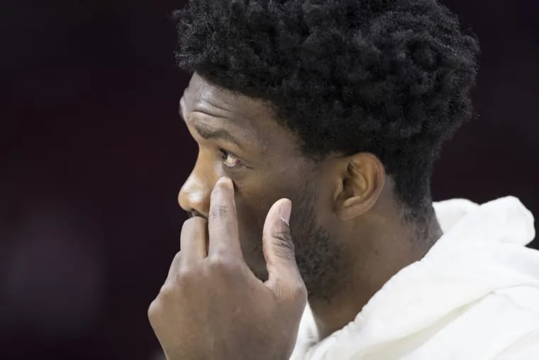 Joel Embiid of the Sixers on the sidelines before their game against the Cavaliers at the Wells Fargo Center on April 6, 2018.  Embiid reaches up to the eye area where he recently had surgery for a fractured orbital.