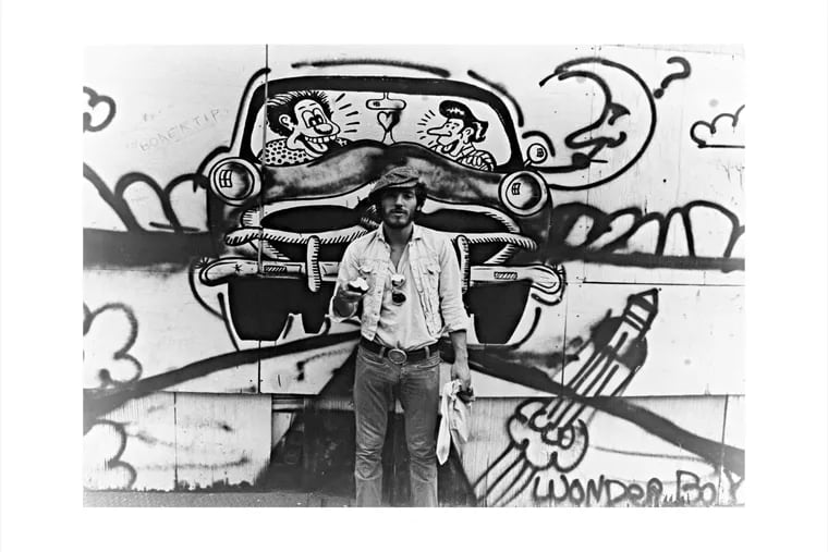 Bruce Springsteen with an apple, standing in front of graffiti on a street in Philadelphia in the 1970s.
