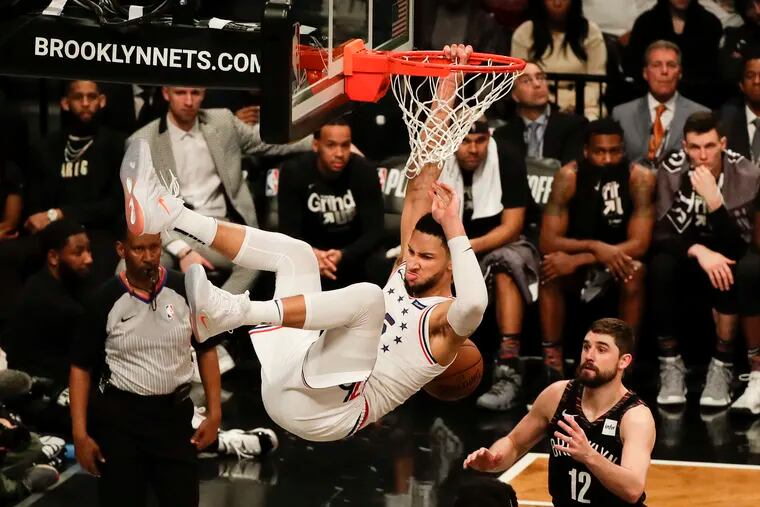 Sixers guard Ben Simmons hangs on the rim after dunking the basketball past Nets guard D'Angelo Russell and forward Joe Harris.
