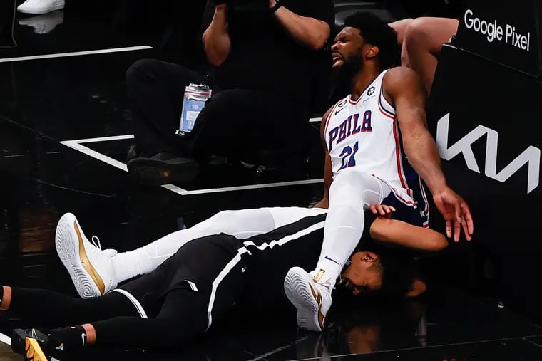 Sixers center Joel Embiid, reacting after he fell over the Nets' Cam Johnson in the third quarter Thursday, will be out with a sprained knee that he suffered during Game 3 as the team tries to sweep the Nets on Saturday.