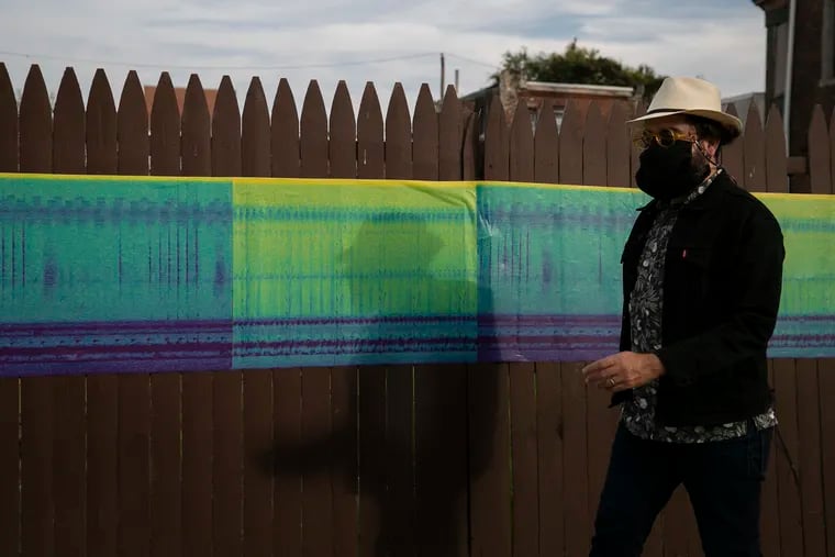 Artist Raúl Romero walks pass printed spectrograms, placed along N. 5th Street near El Centro de Oro, part of his latest exhibit at Taller Puertorriqueño in Fairhill, on Saturday, Oct. 10, 2020.