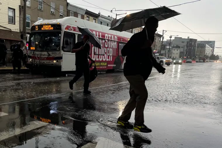 Pedestrians hurry off of a bus during a downpour at the intersection of Girard Avenue and Front Street last month.