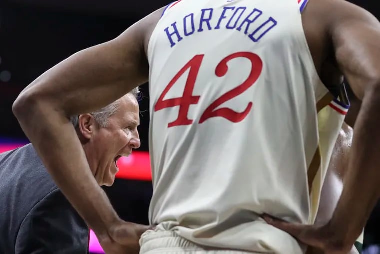 Sixers head coach Brett Brown is seen behind Al Horford as he speaks with the referees in the first half of a game against the Milwaukee Bucks at the Wells Fargo Center on Wednesday, Dec. 25, 2019.
