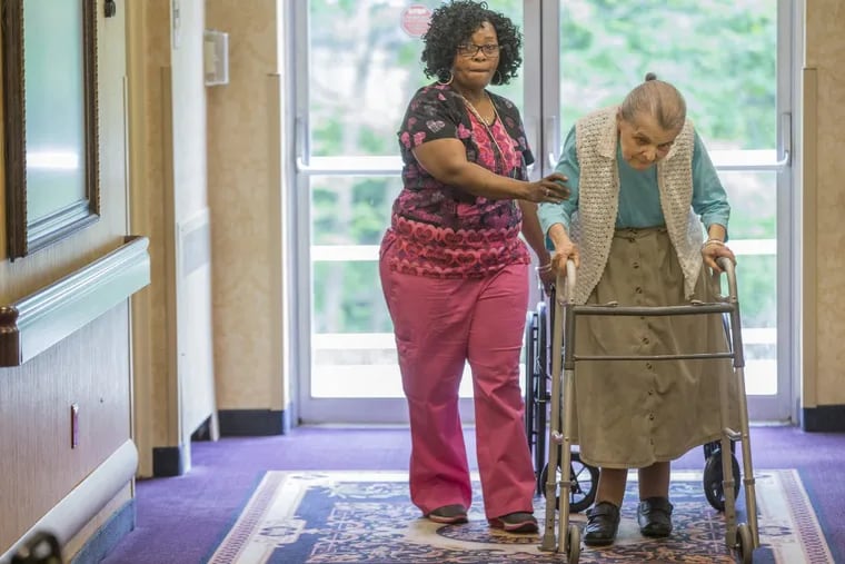 Nurse’s aide Theresa Alston (left) helps resident Ruth Haye down the hall to make sure she gets her daily exercise at Brookside Healthcare Rehabilitation Center near Abington.