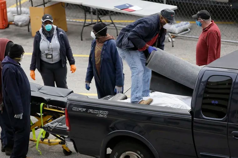 As city workers look on (left) the driver of the pick up truck stands on bodies in truck bed he brough to the Joseph W. Spellman Medical Examiner Building parking lot fenced in area, where there are three refrigerated trailers on April 19.
