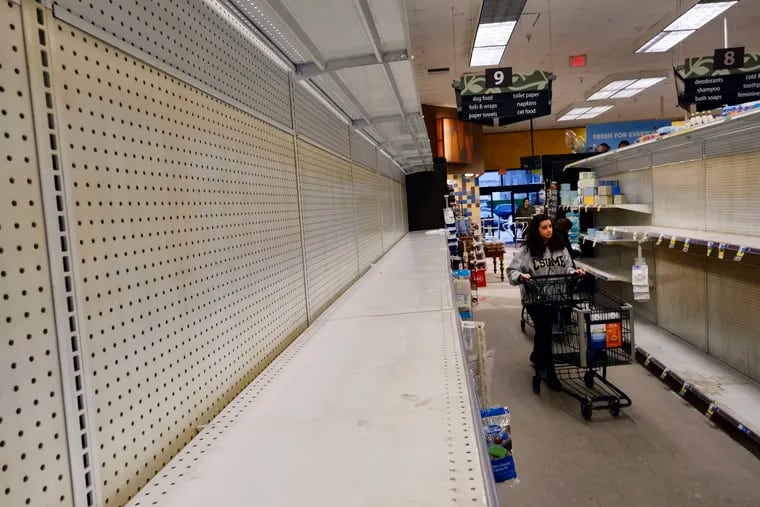 A shopper walks through an empty aisle of shelves of toilet paper and pet foods at a Los Angeles supermarket.