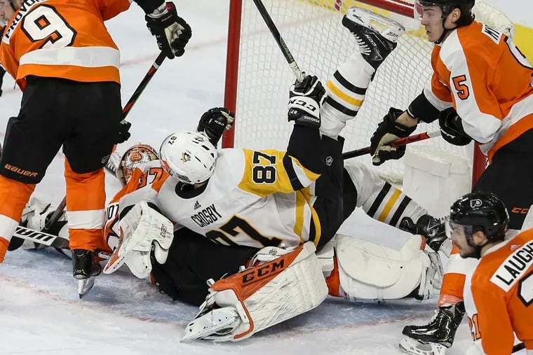 Penguins star Sidney Crosby (87) falls on Flyers goalie Brian Elliott in January. Will the bitter rivals be in the same division is this pandemic-affected season?