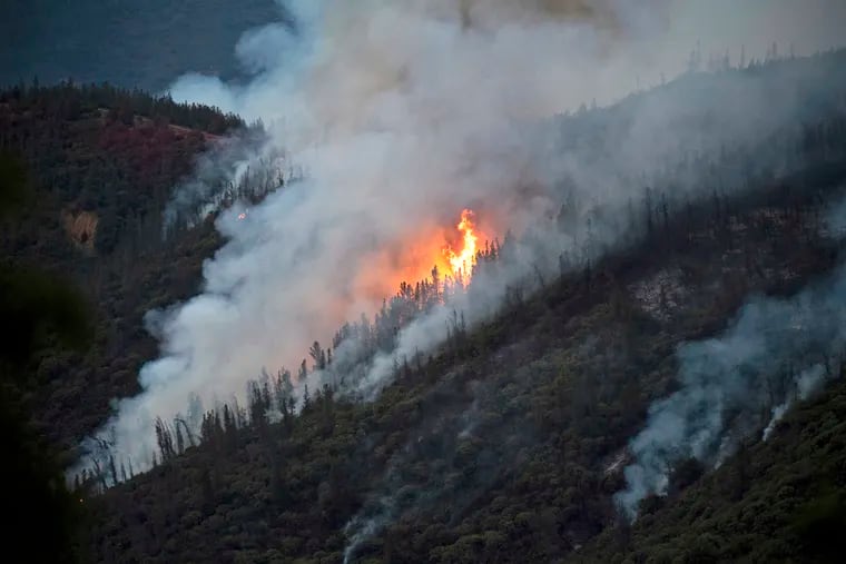 FILE – In this Sunday, July 15, 2018, file photo, flames from a wildfire burn down a hillside in unincorporated Mariposa County Calif., near Yosemite National Park.
