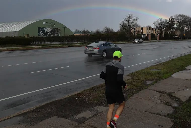 A jogger runs along Pattison Avenue as a rainbow appears after a rain fall in South Philadelphia on Monday, March 27, 2023.