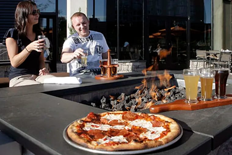 At a fire pit on the rooftop terrace, Natalie Zeppa and Daniel Kalinovski sip from a tasting rack, with a pepperoni pizza near at hand. (AKIRA SUWA / Staff Photographer)
