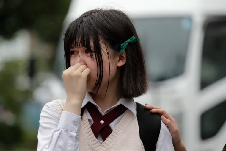 A woman sheds tears as she visits a makeshift memorial honoring the victims of Thursday's fire at the Kyoto Animation Studio building, background center, Friday, July 19, 2019, in Kyoto, Japan. A man screaming "You die!" burst into the animation studio in Kyoto, doused it with a flammable liquid and set it on fire Thursday, killing dozens of people in the attack that shocked the country and brought an outpouring of grief from anime fans.