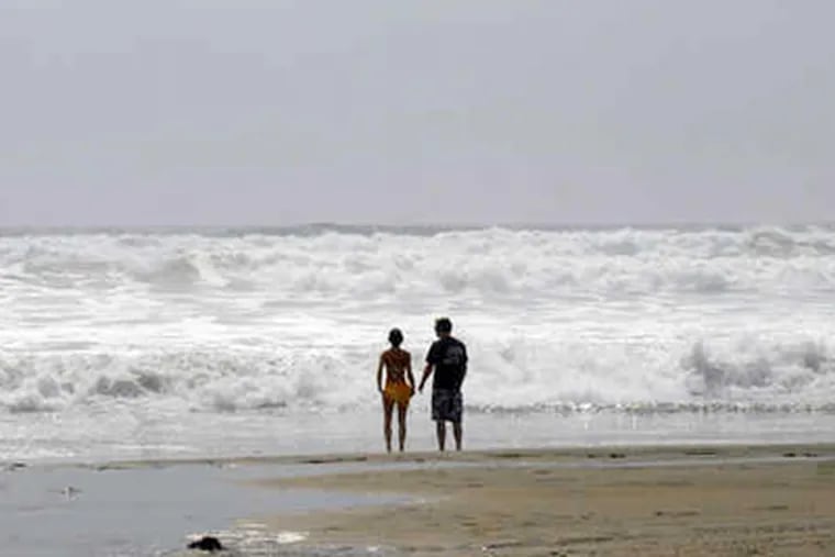 On the beach in Longport, N.J., Jenna Palmisano and Kevin Callender watch rough waters caused by Hurricane Bill. Higher tides in June and July also contributed to unusual coastal conditions. (Ron Tarver / Staff Photographer)