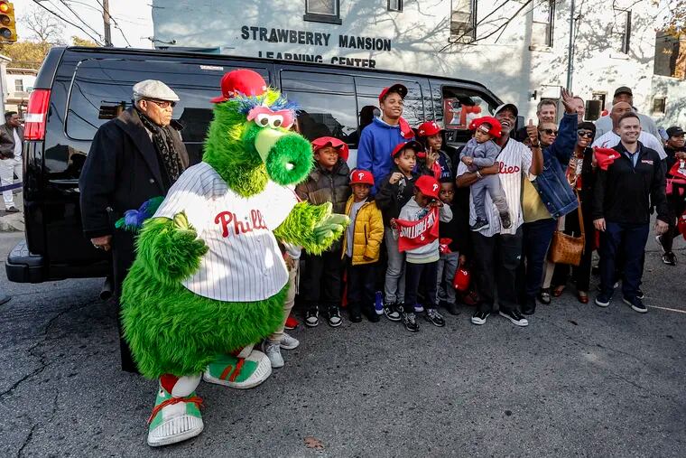 The Phillie Phanatic and former players at the Strawberry Mansion Learning Center pose with children for the donation of a van for the Center's field trips. During the presentation, the Center's founder, Kevin Upshur, (pictured holding a toddler) was called an "MVP of community."