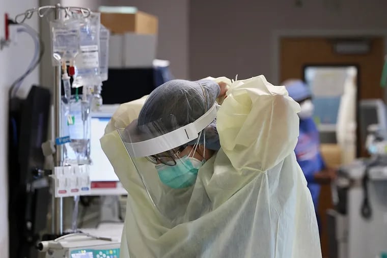 A health-care worker puts on personal protective equipment before entering a patient room inside a COVID-19 intensive care unit at Temple University Hospital's Boyer Pavilion in North Philadelphia in 2020. Hospital leaders say they are seeing patient volumes rise again, often with unvaccinated patients.