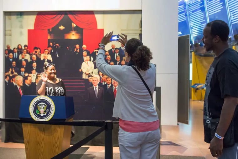 The National Constitution Center, celebrating the document's 227th anniversary, had free admission Wednesday. At the Presidential Oath of Office exhibit, Shawnda Bolden (left) raises her right hand as friends Maria Teresa Del Valle Octavio and Corey Tyrone Jackson capture the moment. New citizens also were sworn in. Story, B6.