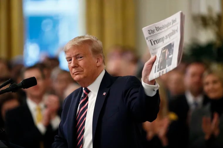 President Donald Trump holds up a newspaper with the headline that reads "Trump acquitted" as he speaks in the East Room of the White House in Washington Thursday.
