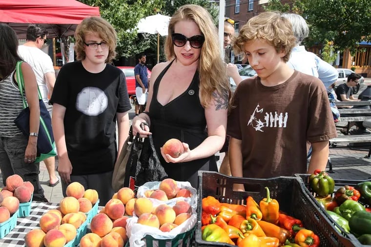 Jenn McCreary, 45, of South Philly, selects peaches with her twin teenage boys, Caleb (left) and Malcolm at the Farmer's Market at Passyunk Avenue and Tasker Street.