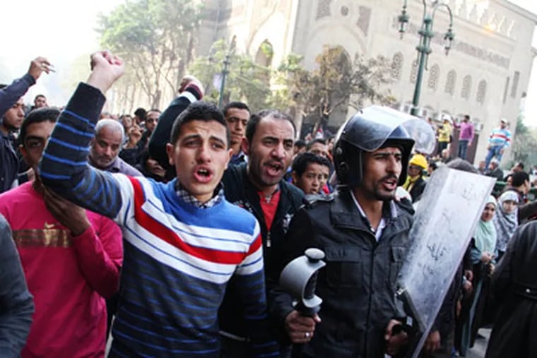 Egyptians, one of them wearing a riot police officer's helmet and carrying a shield bearing the words, "I am the government, I am the military and police, dirty hand", chant slogans during a protest demanding the end to military rule in Tahrir Square, Cairo, Egypt, Monday, Dec. 19, 2011. Hundreds of Egyptian soldiers in riot gear swept through Cairo's Tahrir Square early Monday and opened fire on protesters demanding an immediate end to military rule. (AP Photo)