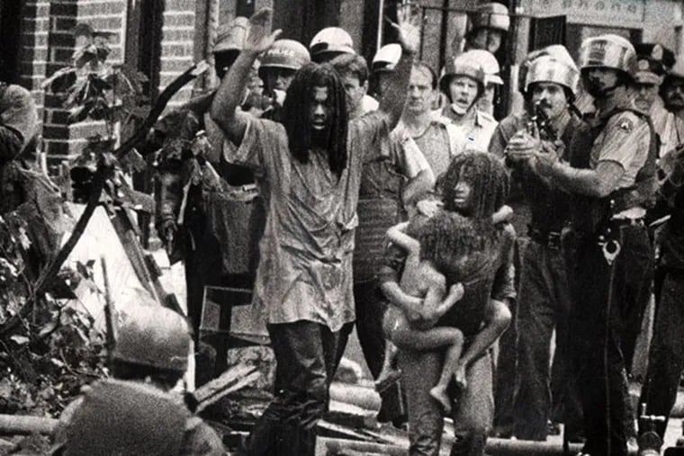 "LET THE FIRE BURN": MOVE members and children emerge from their "headquarters" in a 1978 confrontation. ( Sam Psoras / Philadelphia Daily News )