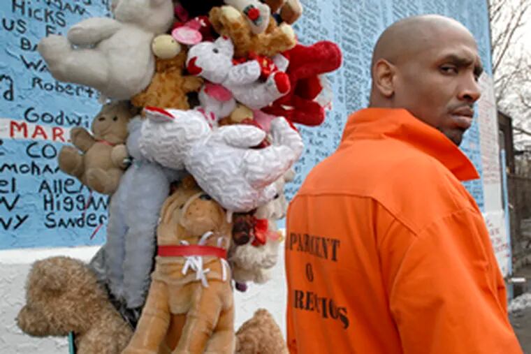 Michael &quot;MIC&quot; Ta&#0039;bon , who has served time, visits the mural in the prison jumpsuit he wears when he works with youngsters. Next to him is the two-story memorial utility pole of stuffed animals.