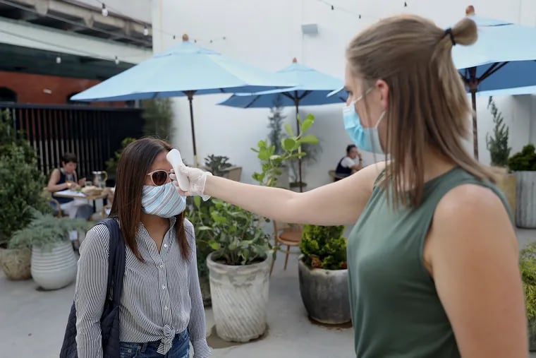 Assistant general manager Phoebe O'Leary (right) uses an infrared thermometer to take Thuy Tran's temperature before she is seated at Suraya in Philadelphia's Fishtown section on Tuesday, Aug. 11, 2020. The restaurant's garden is open for outdoor dining during the coronavirus pandemic.