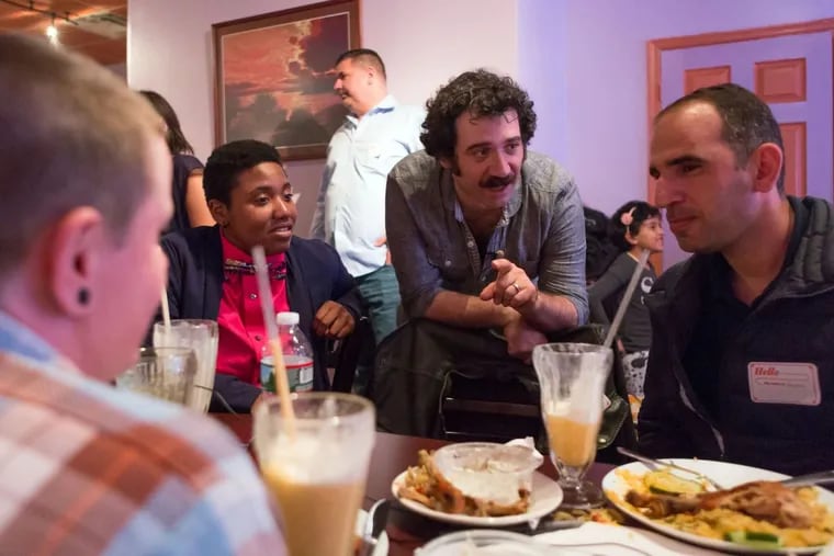 Michael Rakowitz (center, crouching forward) hosts a dinner of American veterans and Iraqi refugees at Amasi restaurant in North Philly. Rakowitz shares stories about the lives of vets and refugees alike in a new weekly radio show, “Radio Silence.”