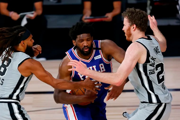 Joel Embiid is defended by San Antonio Spurs' Patty Mills, left, and Jakob Poeltl during the third quarter.