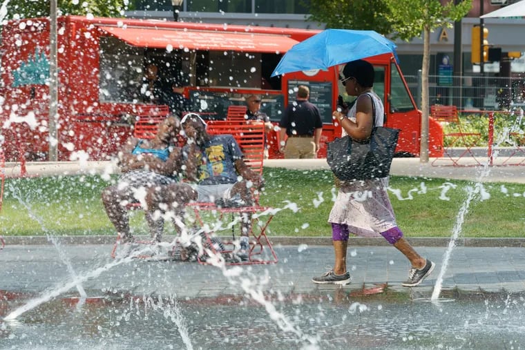 A pedestrian uses an umbrella for shade as she walks through Love Park on a hot summer day.