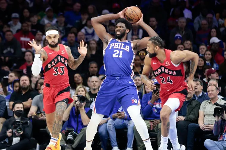 Sixers center Joel Embiid holds up the basketball against Toronto Raptors guard Gary Trent Jr., (left) and center Khem Birch in the first quarter on March 20 in Philadelphia.