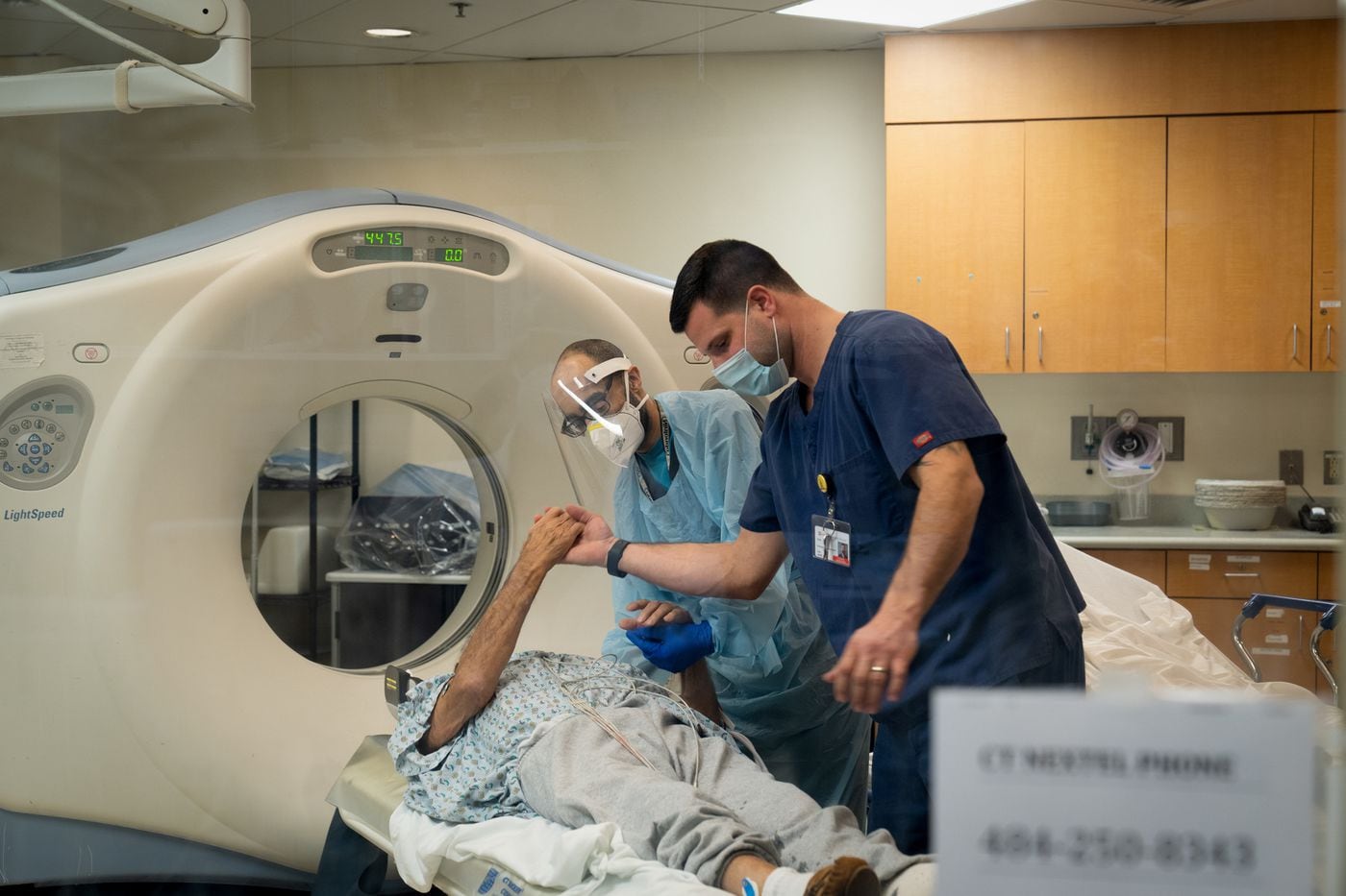 CT technologist Simon Jeffries (back, center) and ER nurse Len Babula (front) perform a CT scan …