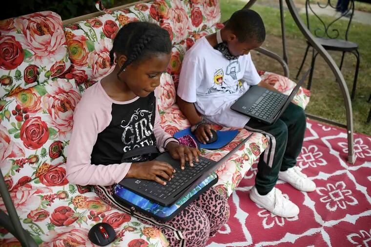 Sammiayah Thompson, left, and her brother, Nehemiah Thompson, work outside in their yard on laptops provided by their school system for distant learning in Hartford, Conn.