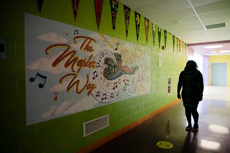 Principal KaTiedra Argro is silhouetted next to a mural dedicated to teacher Mark Maples in the hallway of John Barry Elementary in Philadelphia. Maples was a beloved teacher in the community who died last year of cancer. There are four murals of him around the school.