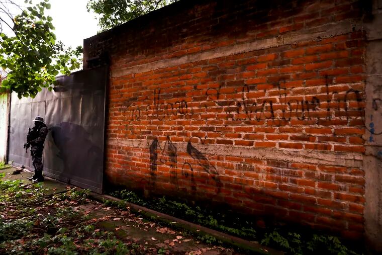 Police guard next to a graffiti wall with the name of a gang as part of a routine patrol in Lourdes, La Libertad, El Salvador. The Human Rights Watch in the report being released Wednesday, Feb. 5, 2020, said that at least 138 people deported to El Salvador from the U.S. in recent years were subsequently killed. The new report comes as the Trump administration makes it harder for Central Americans to seek refuge here.